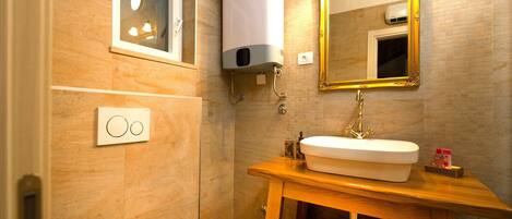 A bathroom with a wooden vanity, a white sink, a gold-framed mirror, and a toilet.