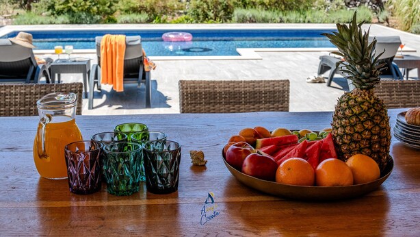 Mesa junto a la piscina con frutero, vasos y jarra.