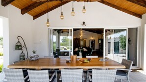 Un comedor espacioso con una gran mesa de madera, sillas de mimbre y lámparas colgantes.