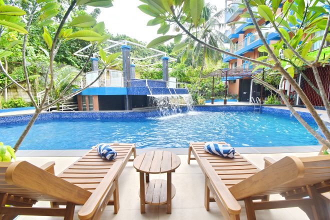 A pool with a waterfall feature, surrounded by wooden lounge chairs and a small table.