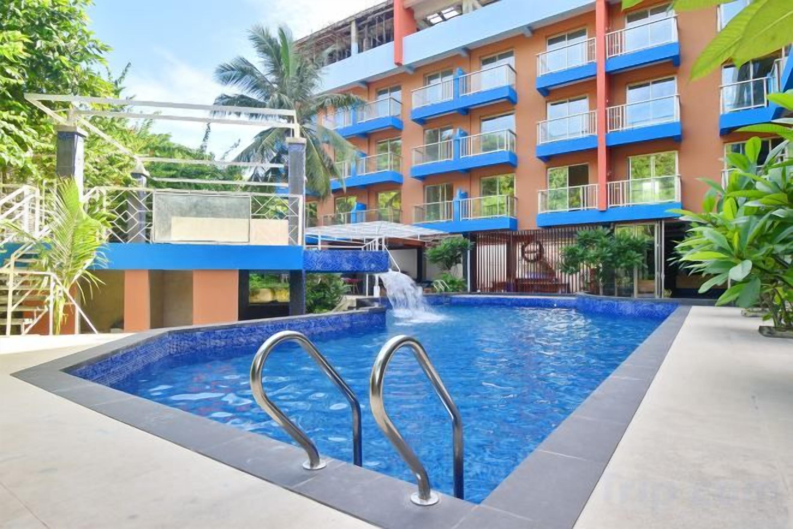 Une piscine agrémentée d’une cascade, entourée d’un hôtel à plusieurs étages doté de balcons.