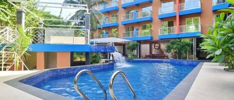 Une piscine agrémentée d’une cascade, entourée d’un hôtel à plusieurs étages doté de balcons.