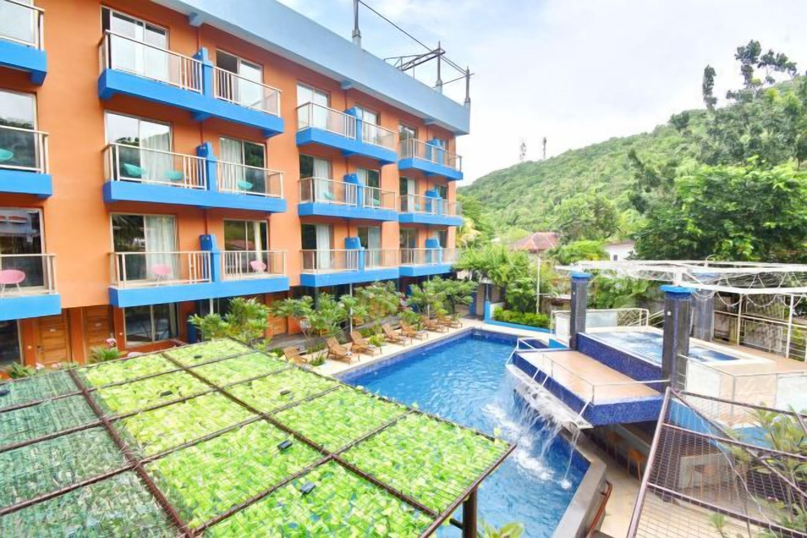 A hotel with a swimming pool, multiple balconies, and a view of a hilly landscape.