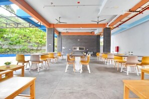 A modern indoor space with tables and chairs arranged for dining, a kitchen area in the background, and a view of greenery outside. - OSEIDON HOTEL BORACAY (Boracay Island)