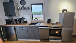 A modern kitchen with grey cabinetry, a wooden countertop, a built-in oven, a dishwasher, and a refrigerator.
