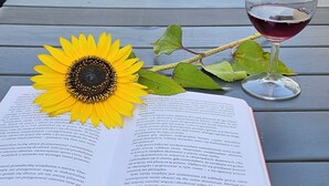 An open book with a sunflower and a glass of red wine on a table outdoors.