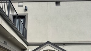 Ein Gebäude mit einer Garagentür, einer schwarzen Haustür mit Hausnummer und einem kleinen Balkon mit Geländer.