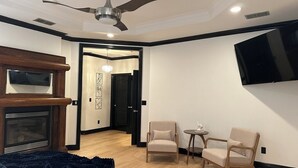 Ein Hotelzimmer mit einem Bett, einem Kamin, einem Deckenventilator, einem an der Wand montierten Fernseher und zwei Sesseln.