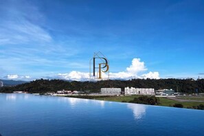 A waterfront property with a large body of water, a clear sky, and a distant building with a prominent 'P' logo. - Paradise Perch Tanjung Aru Inifnity Pool 2BR (Kota Kinabalu)