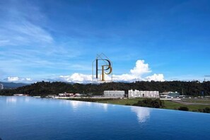 A large body of water with a clear sky, a mountain range in the background, and a building with a prominent 'P' logo. - Paradise Perch Tanjung Aru Inifnity Pool 2BR (Kota Kinabalu)