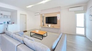 A modern living room with a sofa, coffee table, and a TV mounted on a wooden wall. - Paradise Perch Tanjung Aru Inifnity Pool 2BR (Kota Kinabalu)