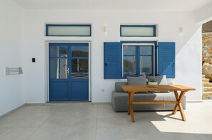 A room with a grey sofa, a wooden table, and two blue doors with shutters.