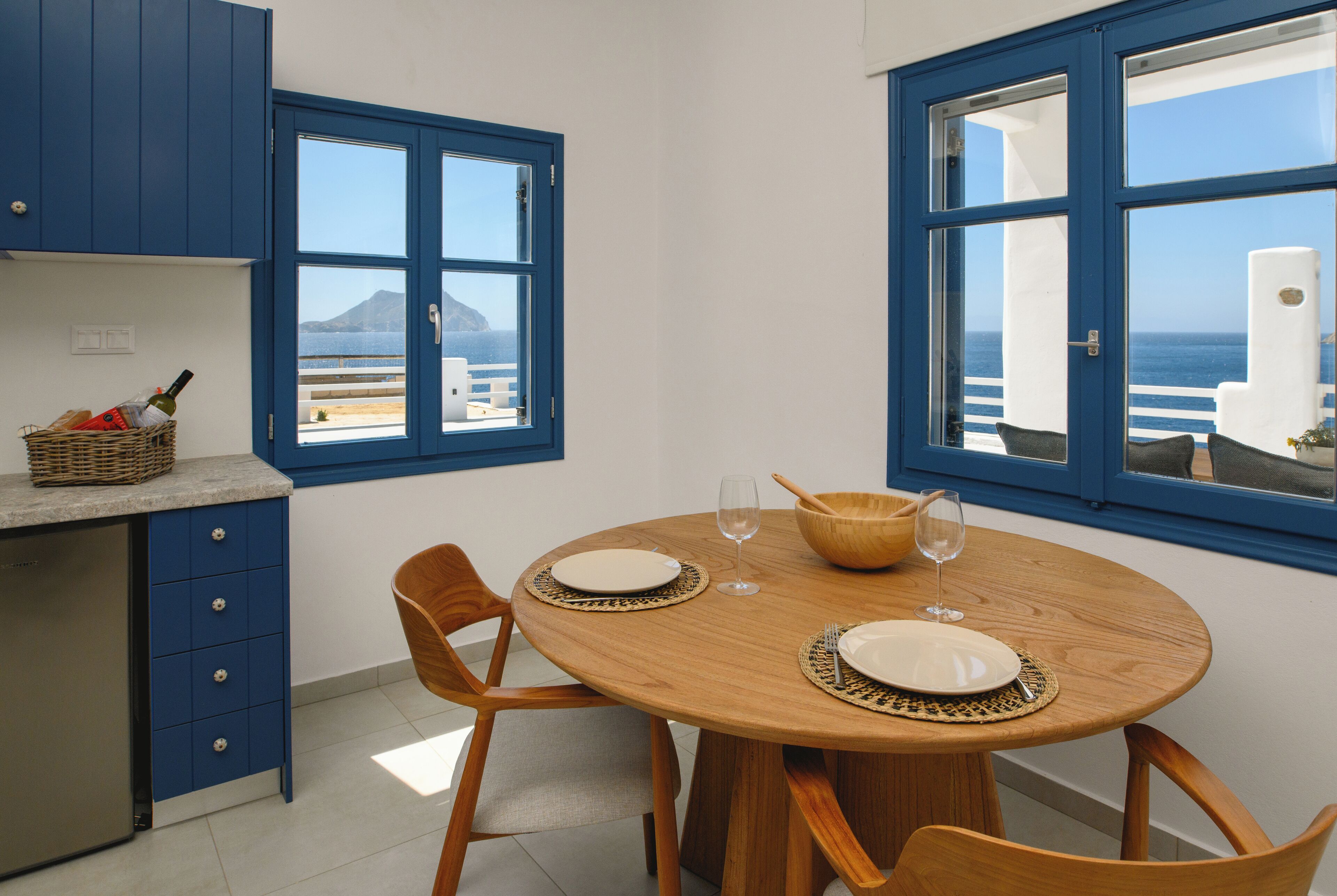 A dining area with a round wooden table, two chairs, and a view of the sea through large windows.