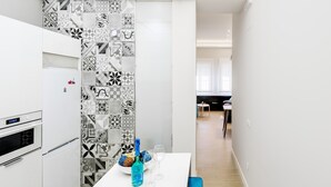 Una cocina moderna con encimera blanca, una silla azul y una mesa de comedor con una botella y vasos.