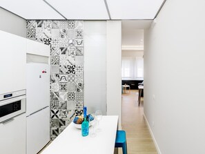 A modern kitchen with a white countertop, a blue chair, and a dining table with a bottle and glasses.