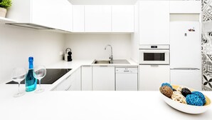 Una cocina moderna con armarios blancos, horno empotrado, lavavajillas y pileta.
