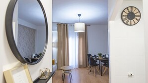 Ett modernt hotellrum med en rund spegel, en matplats med bord och stolar samt en väggklocka.