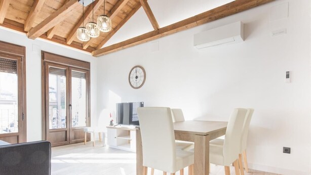 Un espace repas moderne avec une table et des chaises en bois, un téléviseur et une horloge au mur.