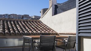 Une terrasse extérieure avec une table et des chaises, un toit en tuiles et une vue sur les bâtiments en arrière-plan.