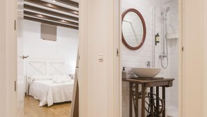 A hotel room with a bed, a bedside table, a mirror, and a bathroom with a sink and shower.