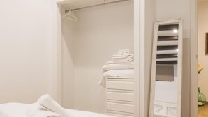 A bedroom with a neatly made bed, a white wardrobe, and a mirror.