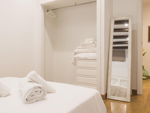 Un dormitorio con una cama bien hecha, un armario blanco y un espejo.