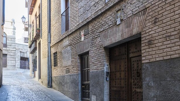 A narrow cobblestone street with traditional brick buildings, a wooden door with a metal lock, and a small window with a metal shutter.