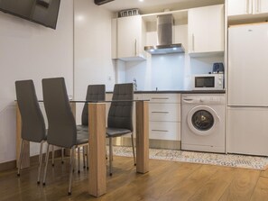 Une cuisine compacte équipée d’un lave-linge, d’un four à micro-ondes et d’un coin repas avec des chaises et une table.