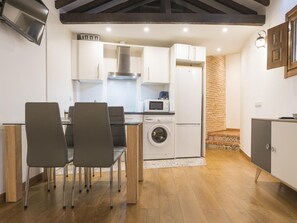 Une cuisine compacte avec des meubles blancs, un lave-linge, un four à micro-ondes et un coin repas équipé de deux chaises.