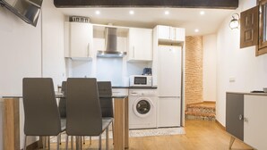 A compact kitchen with white cabinets, a microwave, a washing machine, and a sink. There are two chairs and a small dining table.