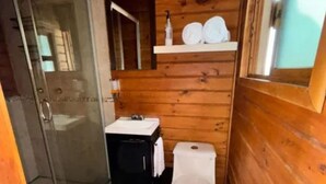 Et lille badeværelse i en træhytte med toilet, håndvask og en brusekabine i glas.