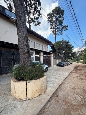 A residential building with a covered driveway, parked cars, and a tree planter with grass. - One-Bedroom Chalet (Valle de Bravo)