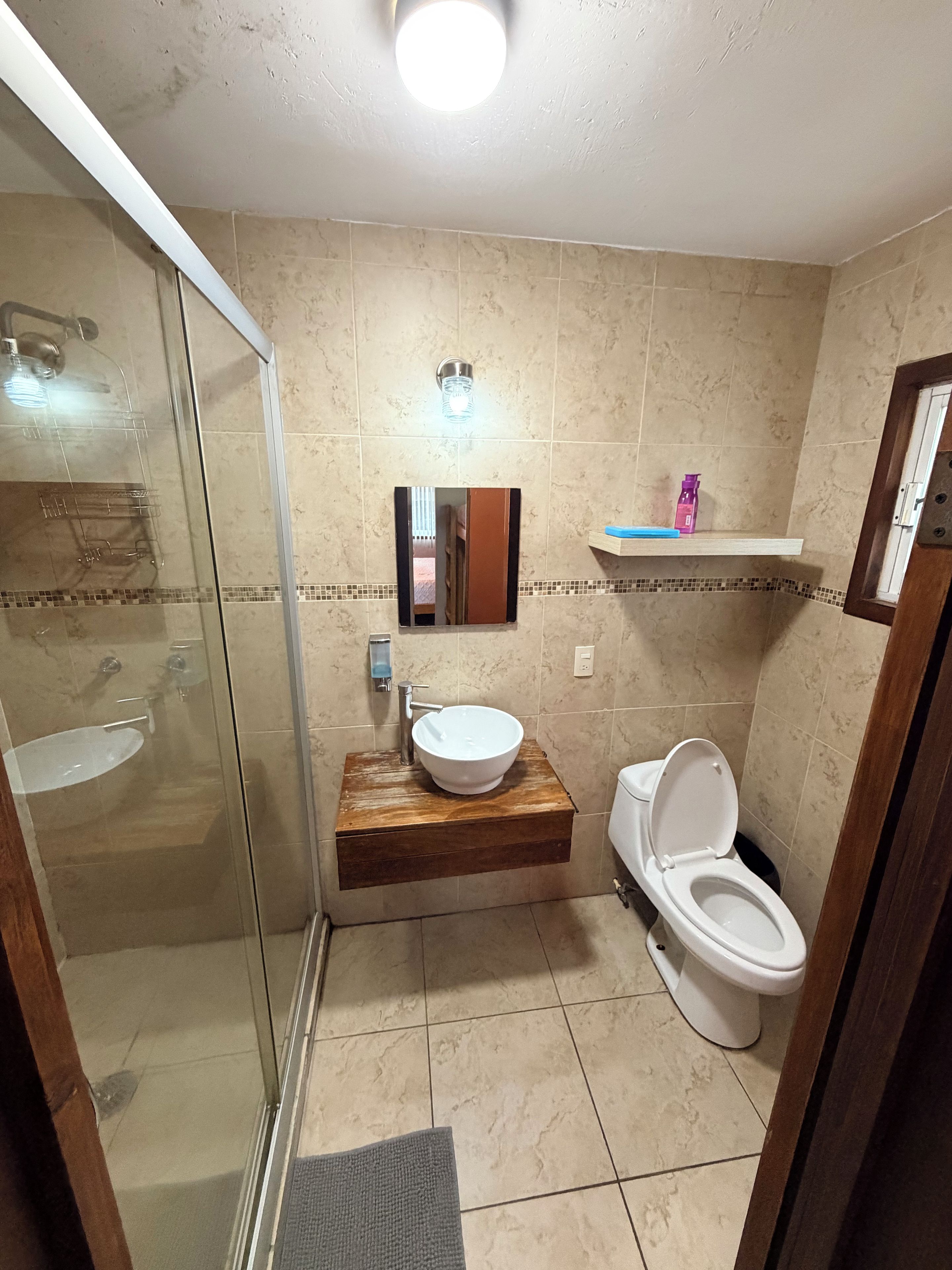 A bathroom with a glass-enclosed shower, a wooden vanity with a sink, and a toilet.
