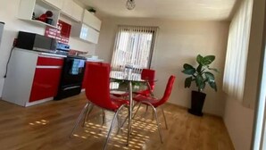 Et kompakt køkken med moderne hårde hvidevarer, et spiseområde med røde stole og en potteplante.