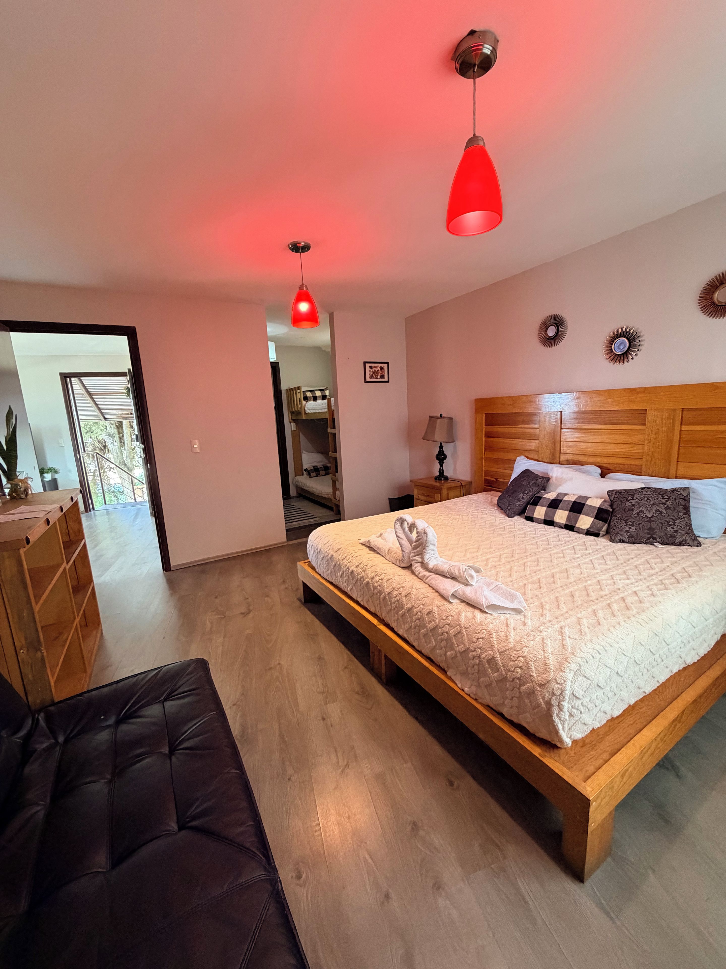 A bedroom with a wooden bed, a red pendant light, a bench, and a view of a balcony.