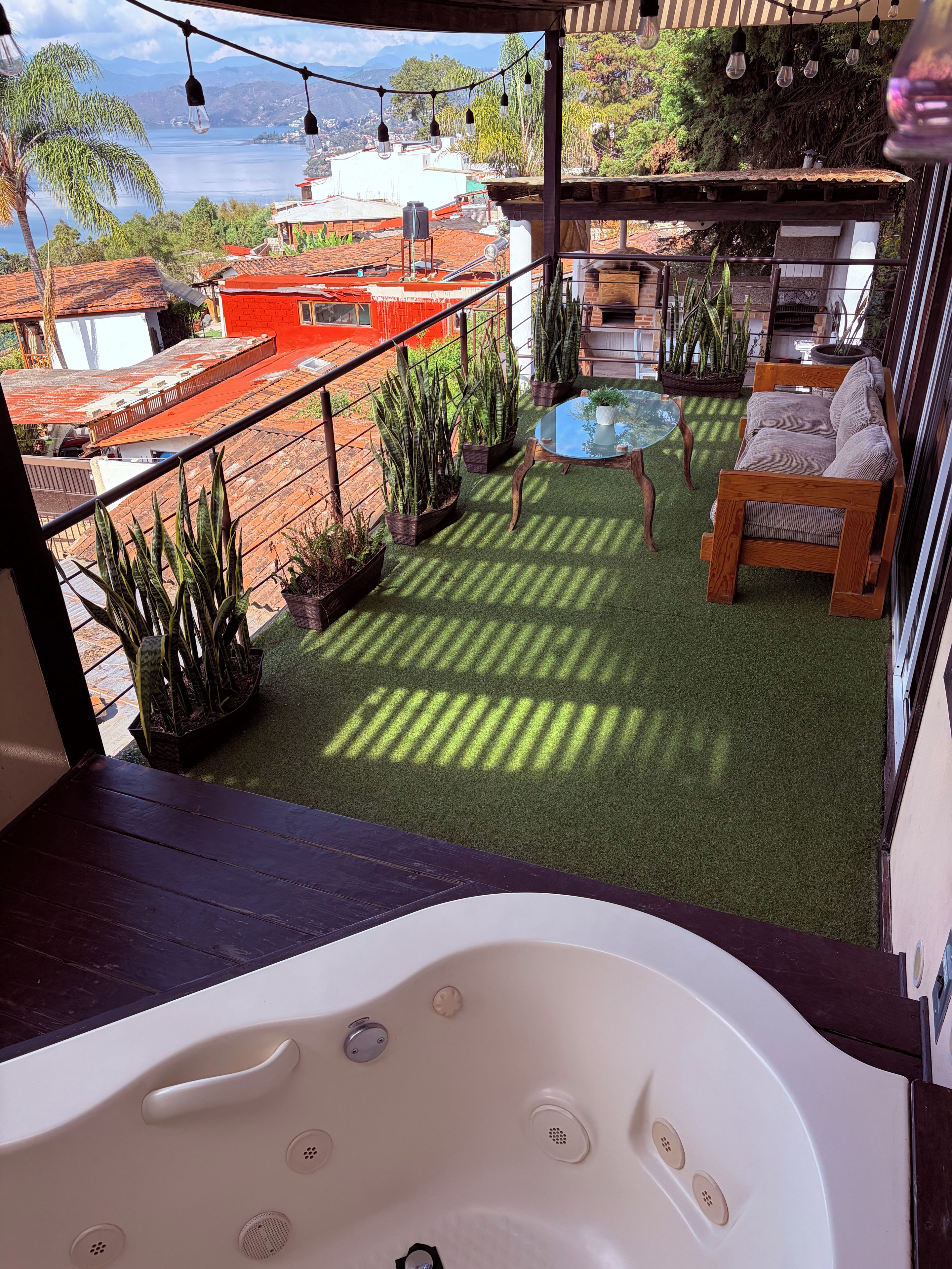 A balcony with a view of a body of water, a hot tub, and potted plants.