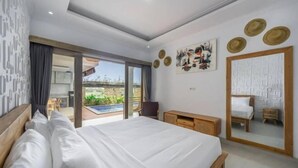 Een moderne slaapkamer met een groot bed, een houten hoofdbord, een bureau en een stoel. Er is een schuifdeur naar een balkon met uitzicht op groen.