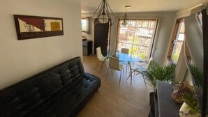 Een woonkamer met een zwarte bank, een eettafel met stoelen en een hanglamp.