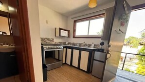 Een kleine keuken met een gasfornuis, spoelbak en een raam voor natuurlijk licht.