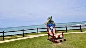A beach chair with a flag design, a palm tree, and a view of the ocean. - Stylish Ocean view w/ HotTub BBQ (Arecibo)