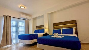 A hotel room with two beds, each with blue bedding and white pillows. There is a window with curtains, a ceiling light, and a wall-mounted air conditioning unit. - Stylish Ocean view w/ HotTub BBQ (Arecibo)