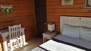 A wooden cabin room with a bed, a small table, a chair, and a nightstand with a lamp. - Cabañas Tr'eje - Double Room (Valle de Bravo)