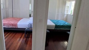 A bedroom with two beds, a bedside table, and a window with shutters. - Villa TERRAVIVA- Saint François  8 pers.- 4 ch- 3 sbb, piscine, WiFi, AC (Saint-François)