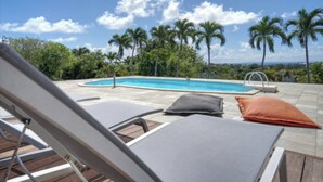 A poolside area with lounge chairs and a swimming pool, surrounded by palm trees and a clear sky. - Villa TERRAVIVA- Saint François  8 pers.- 4 ch- 3 sbb, piscine, WiFi, AC (Saint-François)