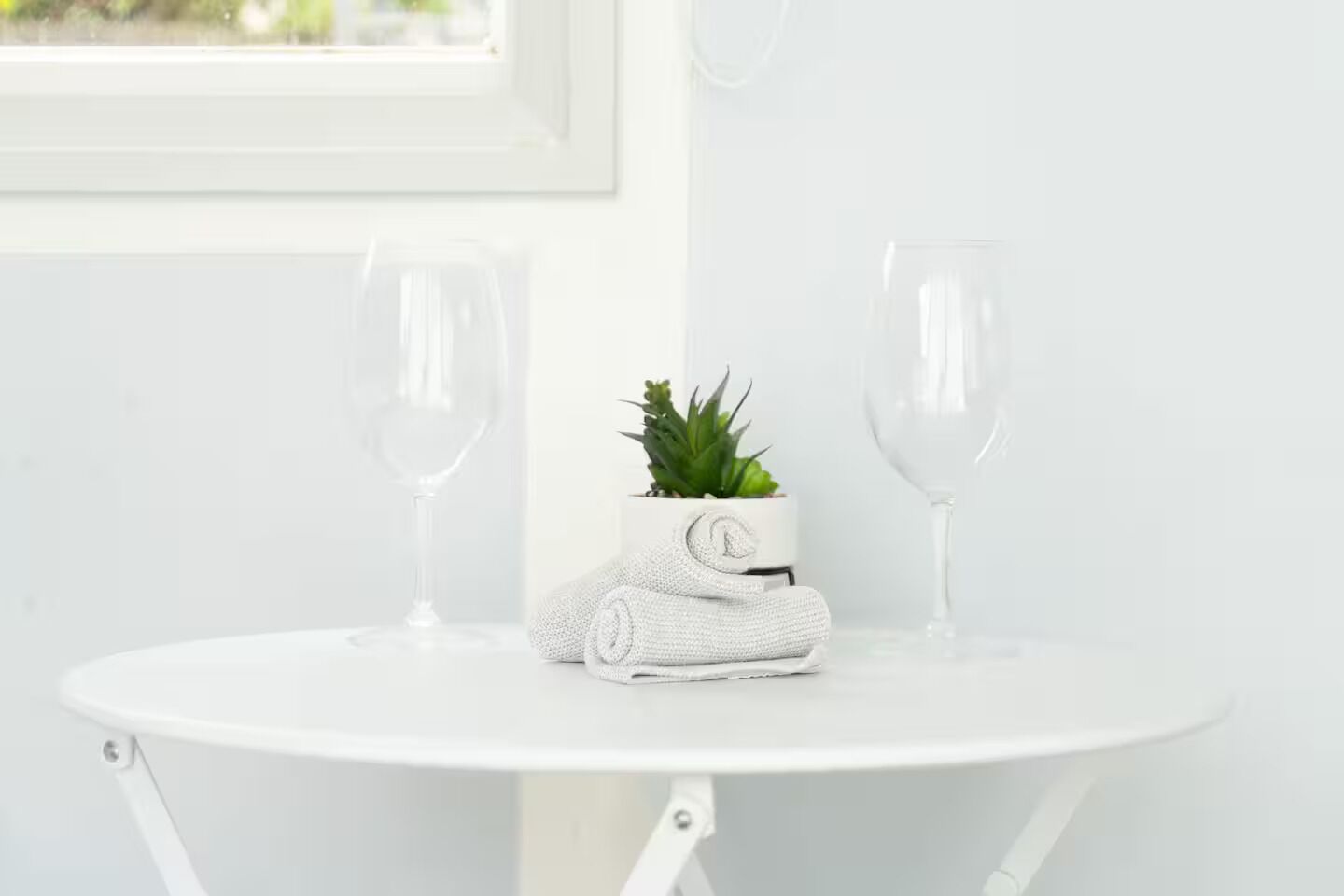 Een witte tafel met twee lege wijnglazen en een kleine potplant met een opgerolde handdoek erop.