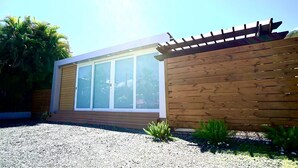 A modern house with a large window, wooden pergola, and a gravel driveway.
