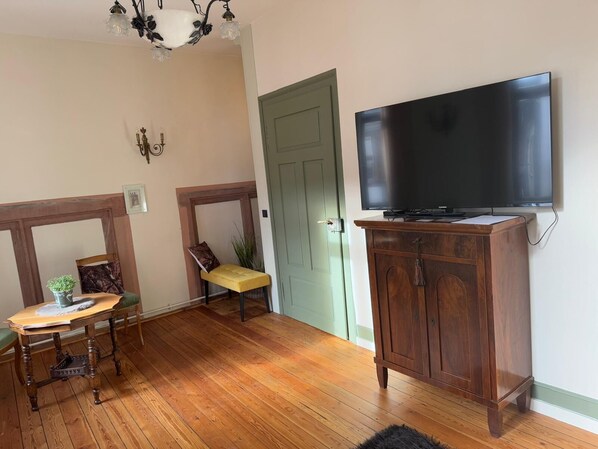 A room with a wooden floor, a television mounted on a cabinet, a door, and a small table with a chair.