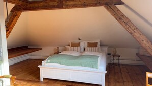 Un dormitorio con una cama blanca, vigas de madera y un suelo con estampado de espiga.