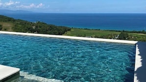 A clear view of a swimming pool with a view of the ocean and a green landscape in the background. - Umarato Villa Sumba (Wanokaka)