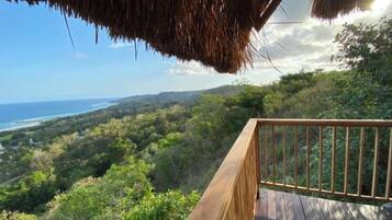 A wooden deck with a railing overlooking a lush green landscape and a view of the ocean.